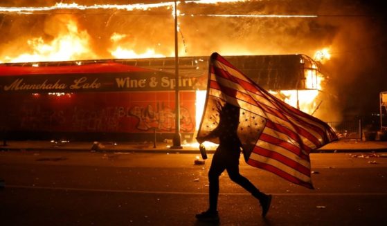A protester carries a U.S. flag upside down, a sign of distress, next to a burning building on May 28, 2020, in Minneapolis during protests over the death of George Floyd.