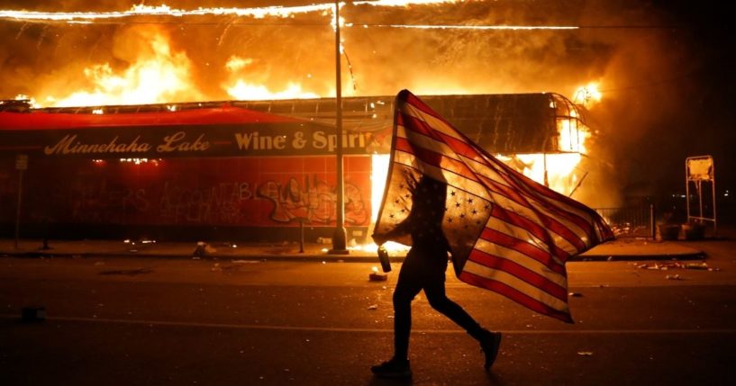 A protester carries a U.S. flag upside down, a sign of distress, next to a burning building on May 28, 2020, in Minneapolis during protests over the death of George Floyd.