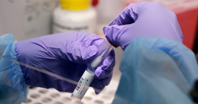A lab worker holds a swab and specimen vial in a COVID-19 testing lab in this file photo from July 2020. Authorities have announced a man in Texas died with COVID, but they have not confirmed whether he actually died 