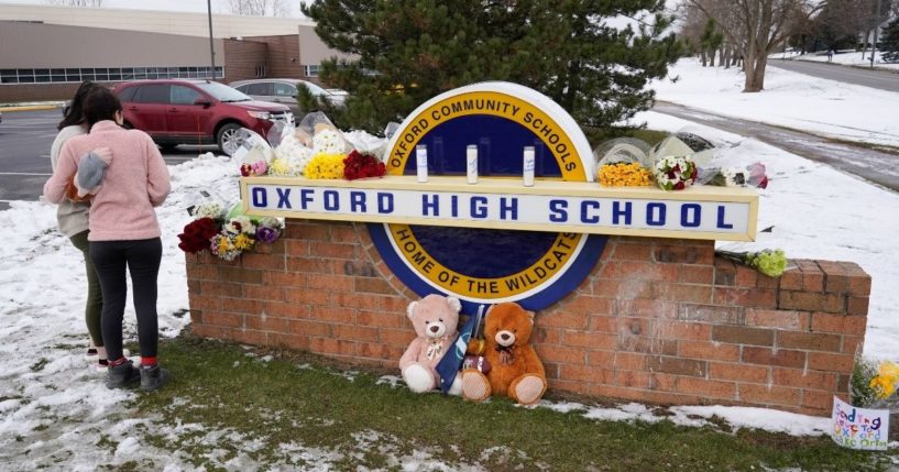 Students stand at the sign of Oxford High School where memorial items are being placed in Oxford, Michigan on Dec. 1.