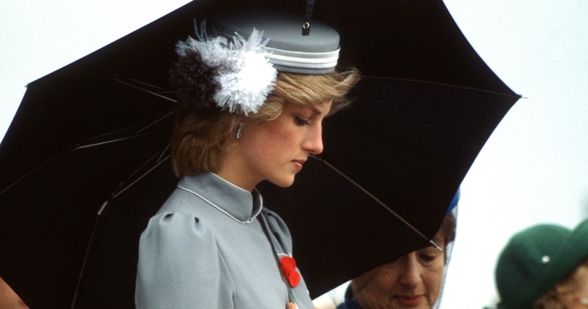 Diana, Princess of Wales, wearing a grey belted dress and a matching bell-boy style hat with feathers, holds an umbrella as she attends an Anzac Day Commemorative Service on April 25, 1983, in Auckland, New Zealand.