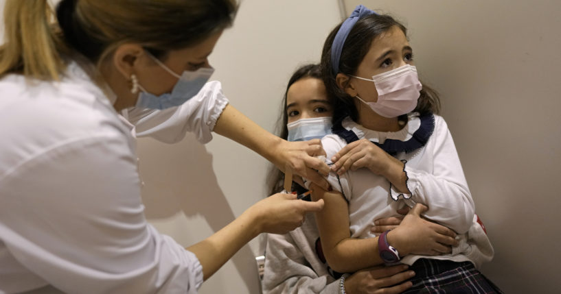 An 8-year-old girl sits on the lap of her sister, 11, while a nurse administers a dose of a COVID-19 vaccine in Portugal on Dec. 18, 2021.