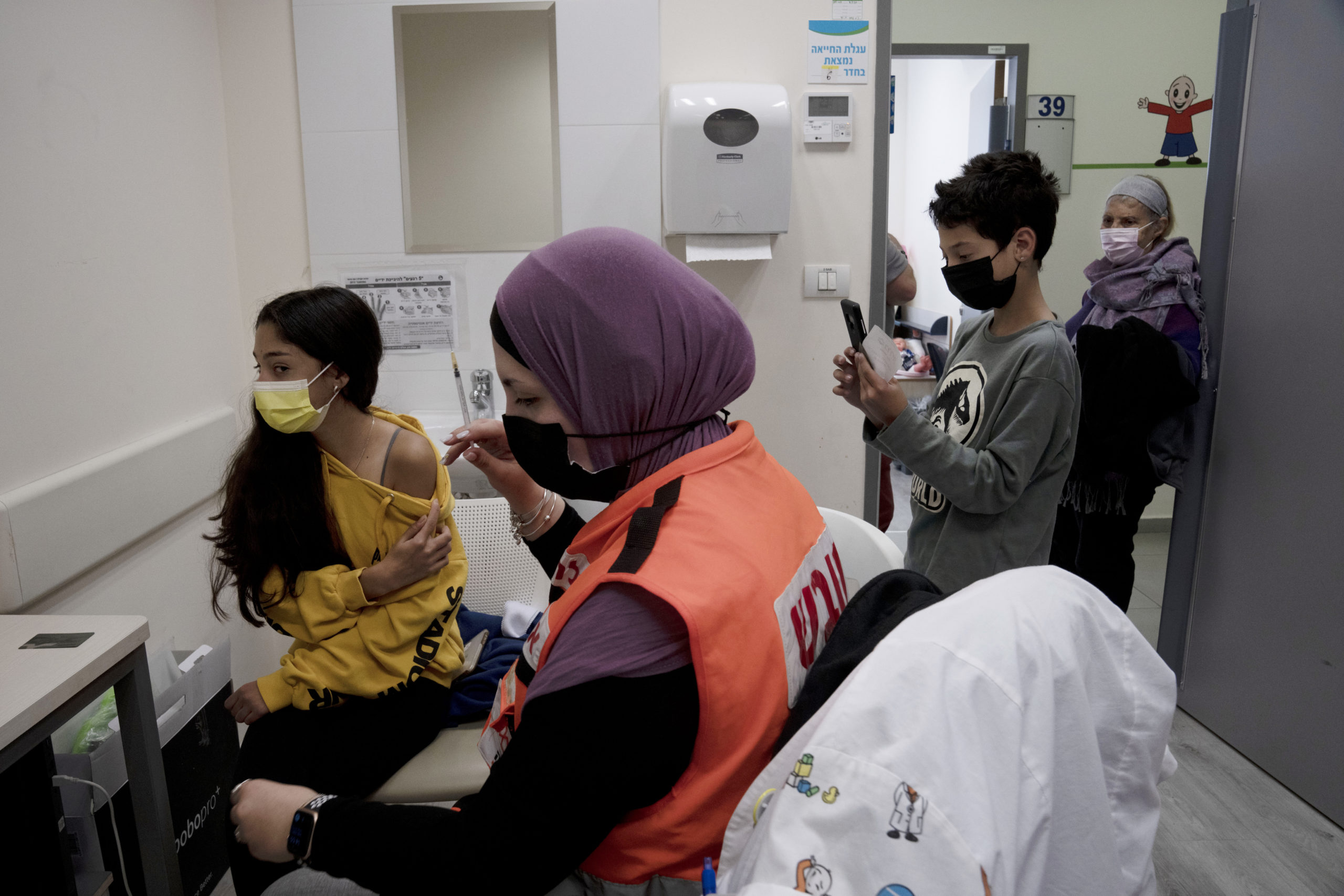 N'amah Yetzhak Abohaikal, a volunteer with the women's unit of United Hatzalah emergency service in Israel, prepares to administer a COVID-19 vaccine to a teen girl as her brother and grandmother watch on Jan. 11, 2022.