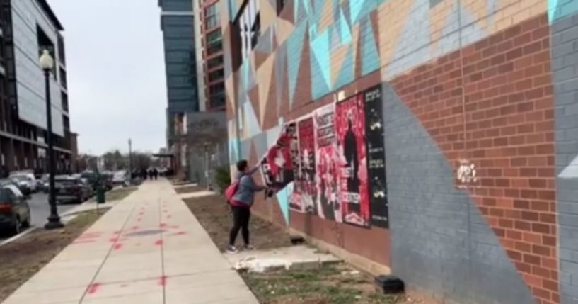 After a series of posters that criticized President Joe Biden appeared in Washington, D.C., a woman can be seen ripping them from the walls.