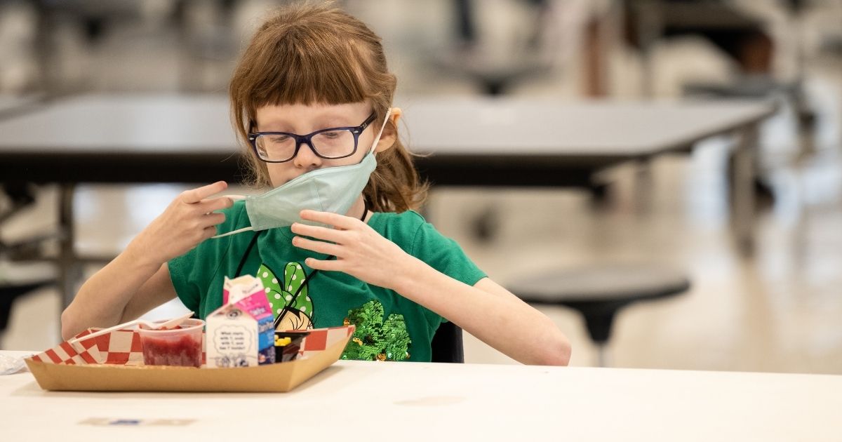 A child puts her mask back on after finishing lunch at a socially distanced table in the cafeteria of Medora Elementary School in Louisville, Kentucky, in this file photo from March 2021. A group of top doctors wrote an opinion piece for The Washington Post, calling for schools to drop mask mandates.