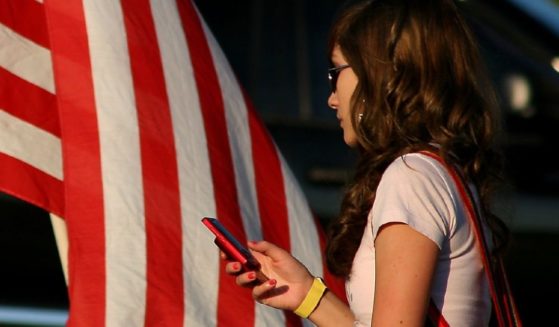 A woman checks her cell phone in front of an American flag.