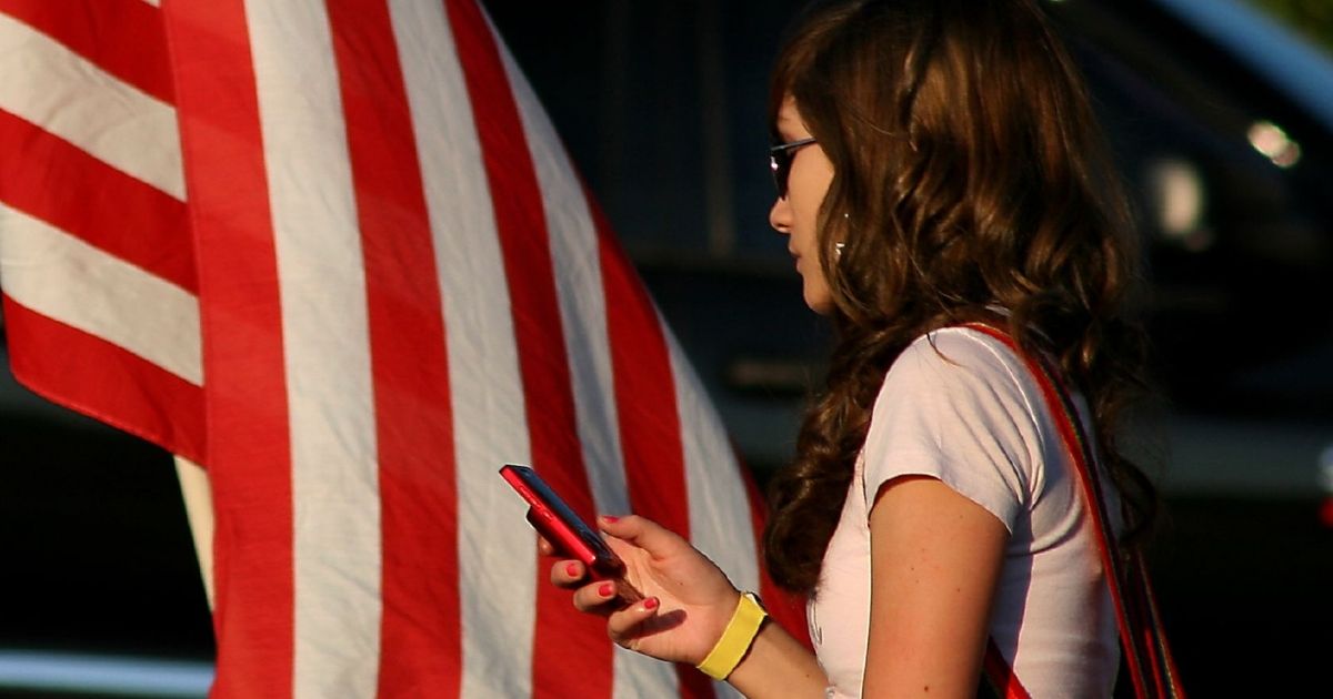 A woman checks her cell phone in front of an American flag.