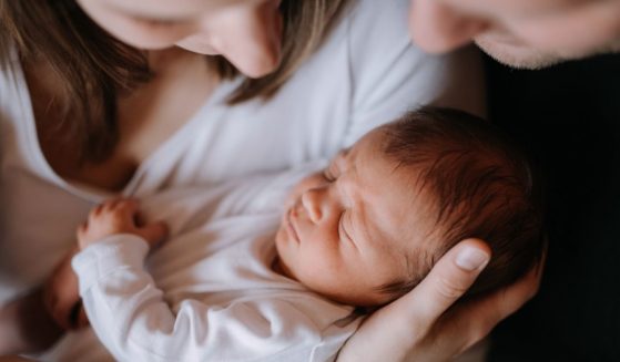 A mother and father hold a newborn baby in the above stock image.