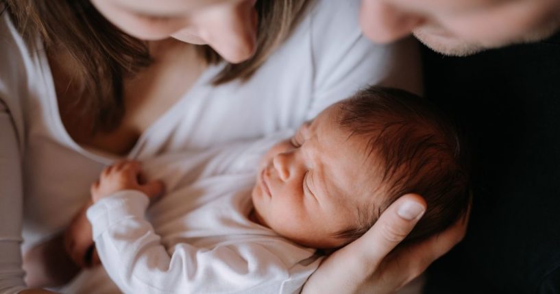 A mother and father hold a newborn baby in the above stock image.
