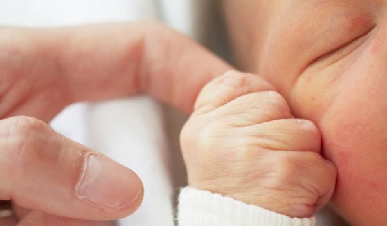 A baby holds a man's finger in this stock image.