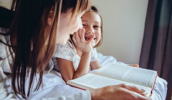 A mother and child read a book in this stock image.