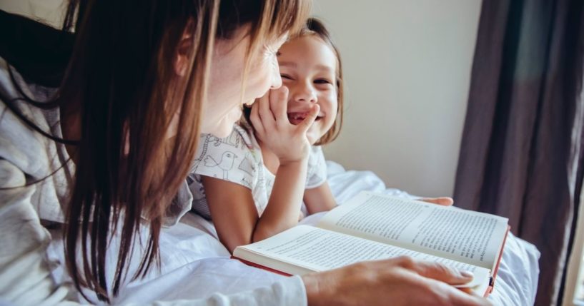 A mother and child read a book in this stock image.