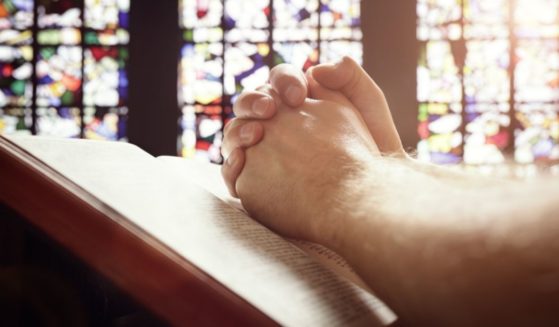 A man folds his hands in a church in the above stock image.