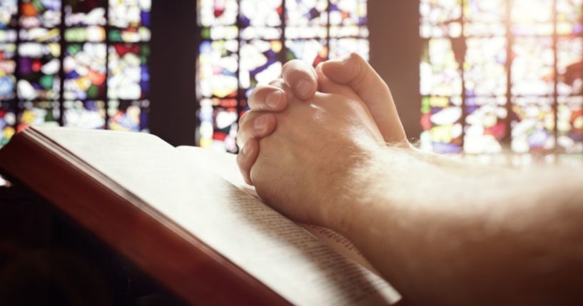 A man folds his hands in a church in the above stock image.