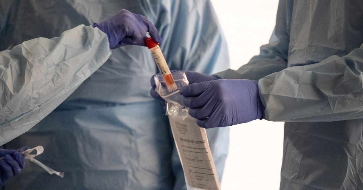 Nurses wearing protective clothing handle a vial containing a COVID-19 test swab at a drive-by testing center at the University of Washington Medical Center campus in Seattle on March 13, 2020.