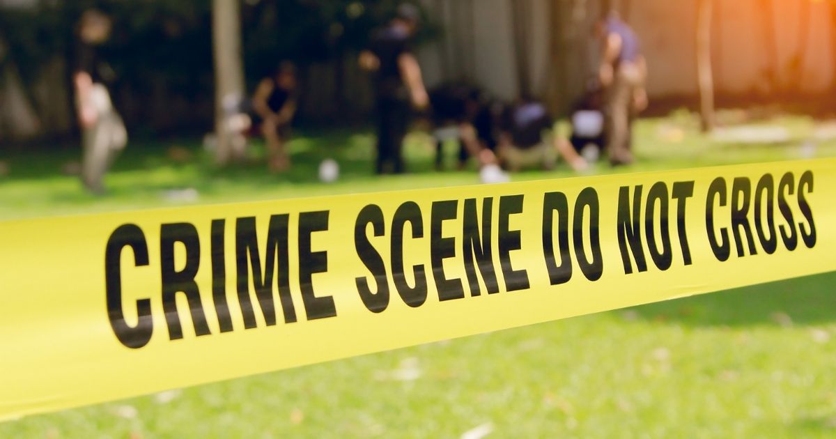 Crime scene tape with a blurred law enforcement team in the background.