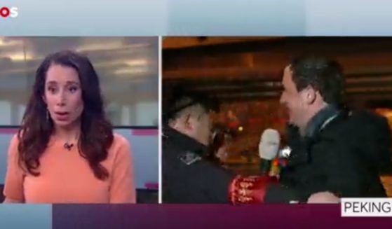 A stunned news anchor looks on, left, as a Dutch journalist's live broadcast is interrupted by a black-coated Chinese security guard, who grabs the man and tries to pull him off camera.