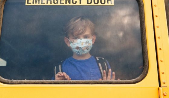 A boy wearing a mask looks out the window of a school bus in this stock image.
