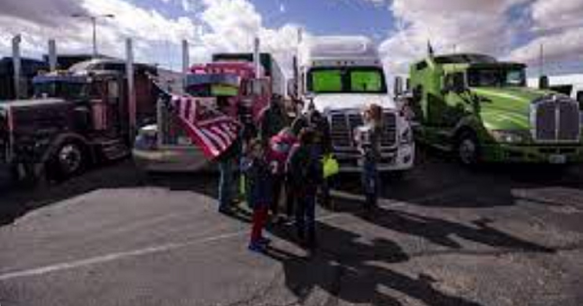 A small group waves American flags in front of parked trucks.