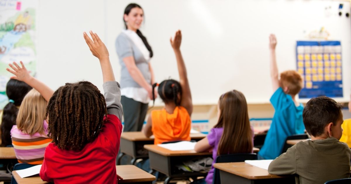 Children raise their hand in a classroom in this stock image.