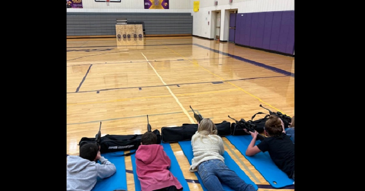 Prone students fire air rifles in a school gym.