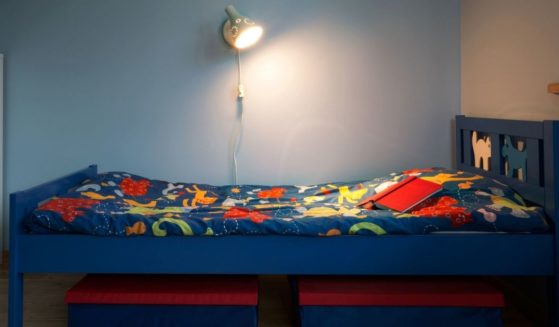 A light shines on an empty child's bed with colorful sheets.
