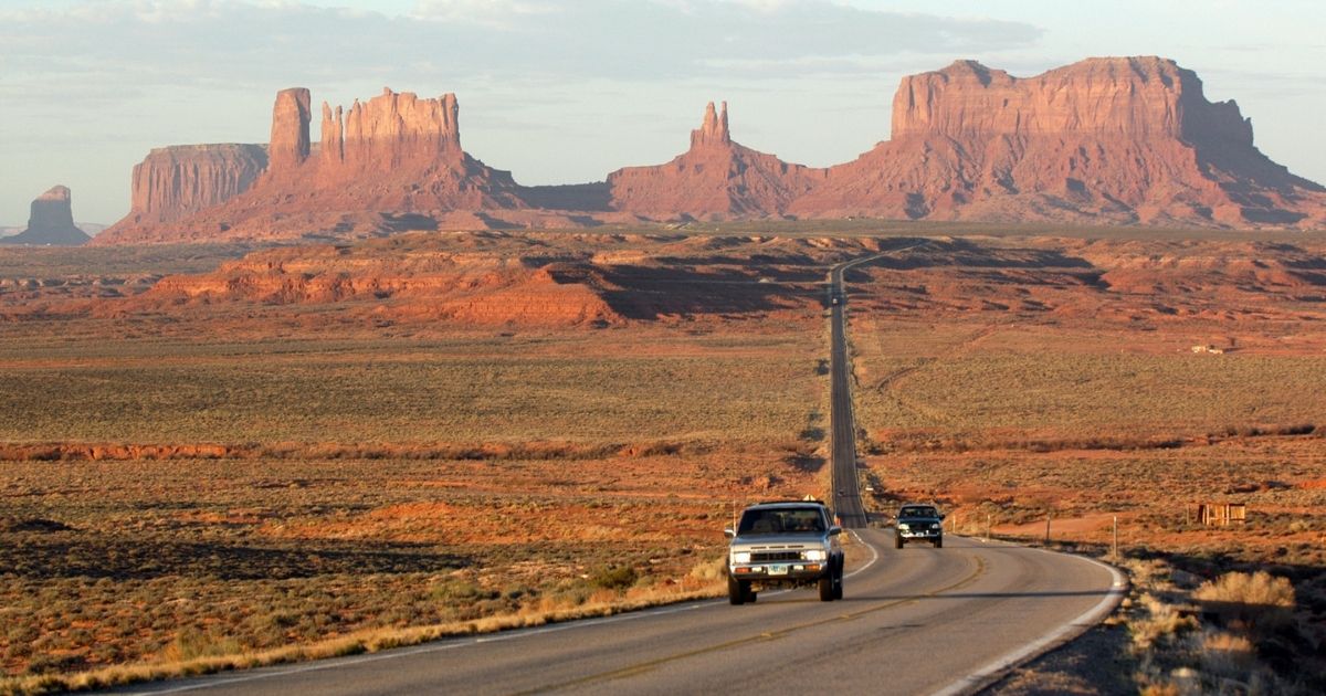 Cars drive away from Monument Valley in Arizona and Utah at dawn.