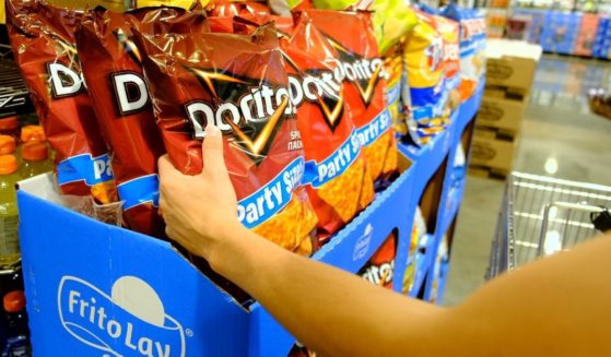 A woman's arm picks up Doritos bag on a supermarket shelf.