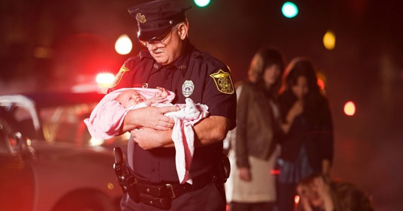 This stock image shows an officer rescuing a baby from the scene of a car accident.