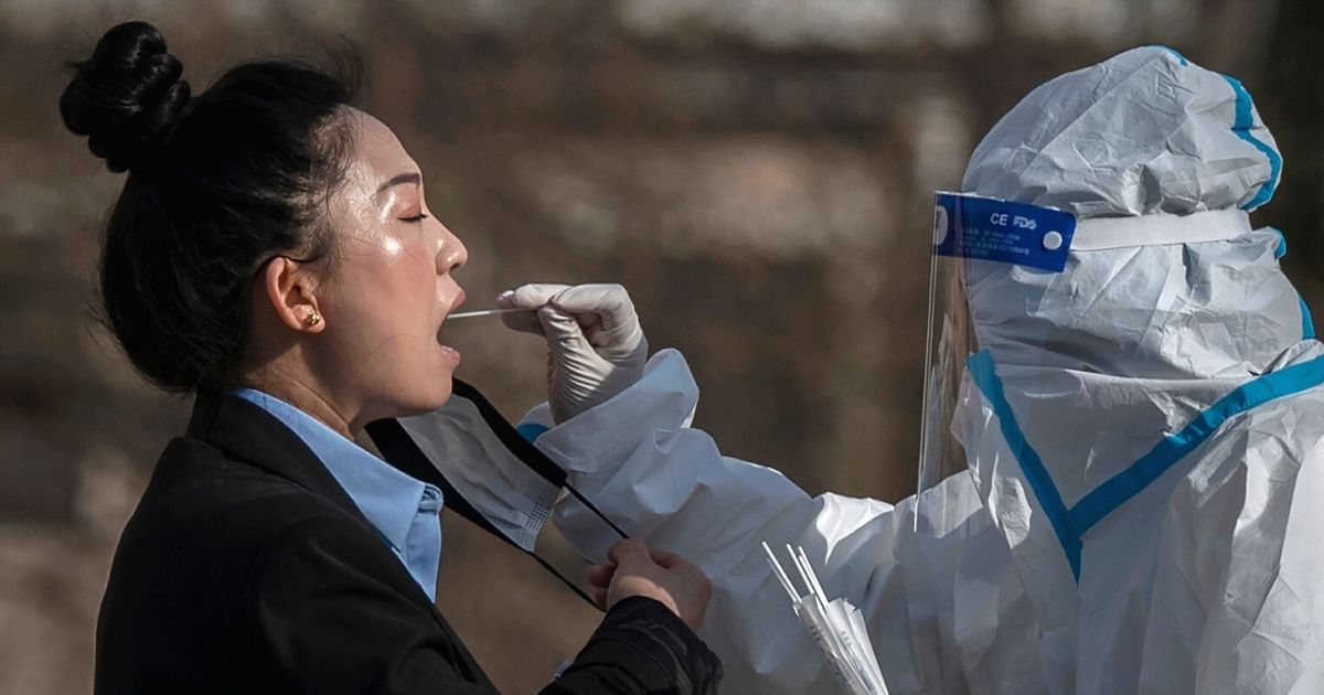 A health worker wears protective gear as she gives a COVID-19 test to a local resident at a mass testing site in Beijing on Wednesday.
