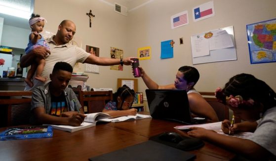 Robert Brown holds his youngest child, Lucy, 9 months, as he and wife, Arlena, center, lead their other children, from left, Jacoby, 11, Felicity, 9, and Riley, 10, through math practice at their home in Austin, Texas, on July 13, 2021.