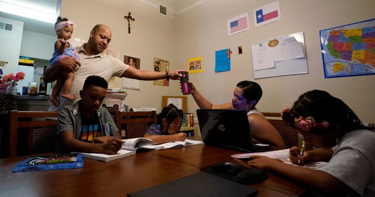 Robert Brown holds his youngest child, Lucy, 9 months, as he and wife, Arlena, center, lead their other children, from left, Jacoby, 11, Felicity, 9, and Riley, 10, through math practice at their home in Austin, Texas, on July 13, 2021.