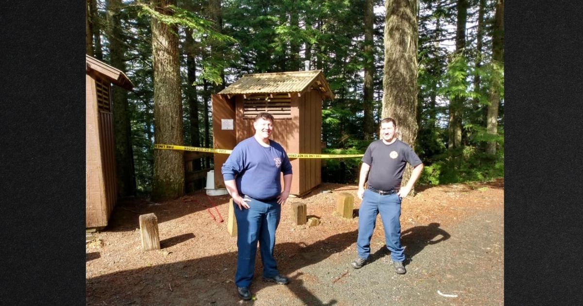 Firefighters pose in front of the park's vault toilets after rescuing a woman who fell headfirst into one while trying to retrieve her cellphone.
