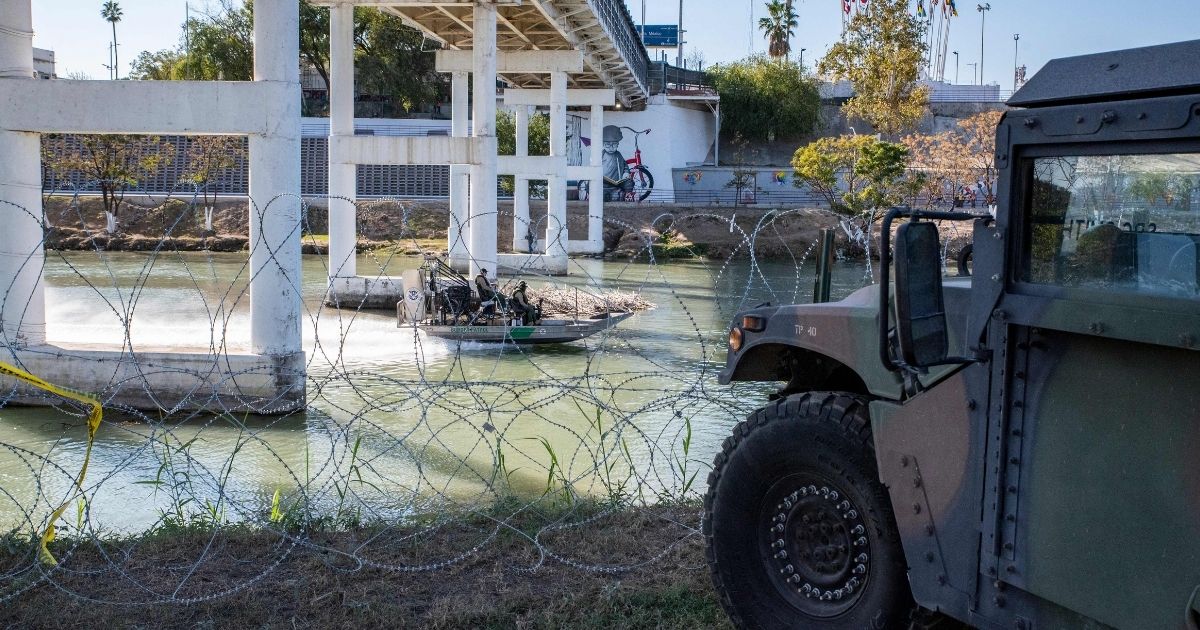 A Customs and Border Patrol boat travels past razor wire and a military vehicle in a file photo from November 2021. The Texas National Guard has been assisting at the Mexico border to help deal with a huge influx of illegal immigrants. Fox News reported today that a Texas guardsman had drowned while attempting to help migrants struggling in the water.