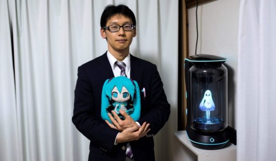 Akihiko Kondo poses next to a hologram of Japanese virtual reality pop singer Hatsune Miku as he holds the doll version of her at his apartment in Tokyo on Nov. 10, 2018, a week after marrying her.