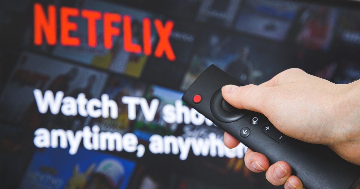 A person uses a TV remote to turn on Netflix.