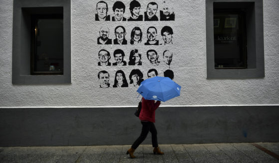 A woman shelters from the rain under an umbrella, while walking past a wall painted with portraits of prisoners of the Basque separatist armed group ETA, in the small village of Hernani, Spain, on May 2, 2018.