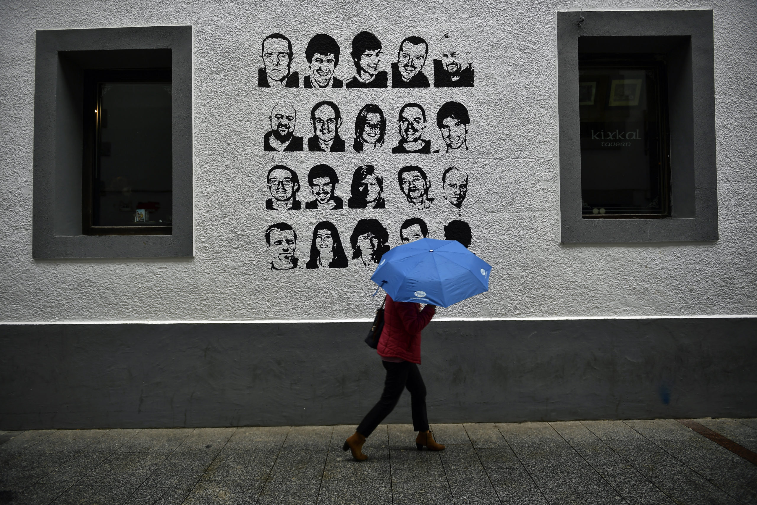 A woman shelters from the rain under an umbrella, while walking past a wall painted with portraits of prisoners of the Basque separatist armed group ETA, in the small village of Hernani, Spain, on May 2, 2018.