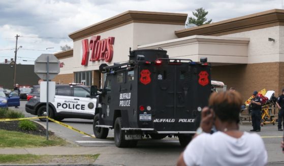 Buffalo police officers shut down the crime scene at the Tops Friendly Market after a mass shooting on Saturday while several people look on.