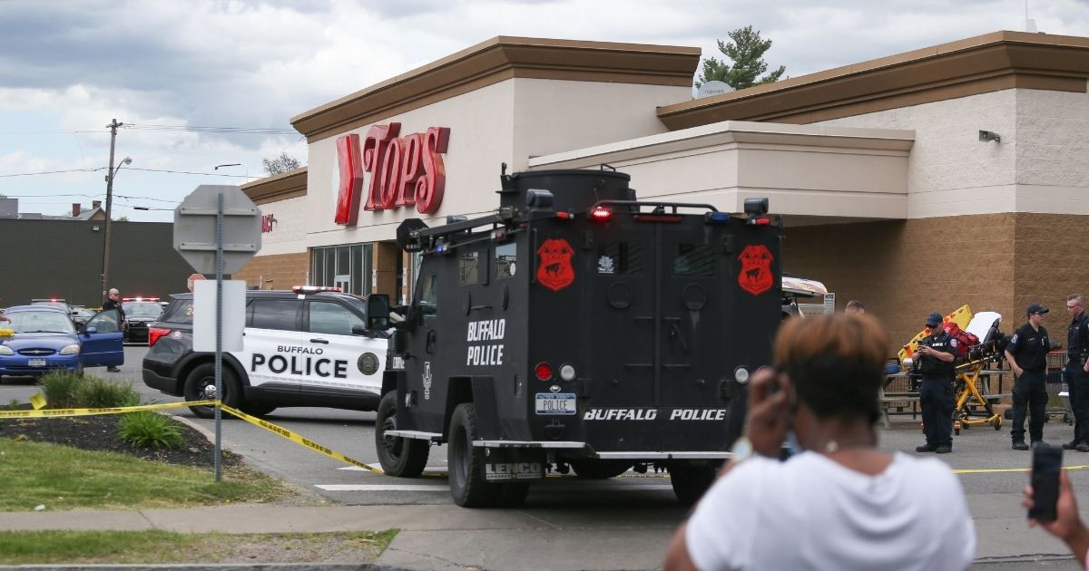 Buffalo police officers shut down the crime scene at the Tops Friendly Market after a mass shooting on Saturday while several people look on.