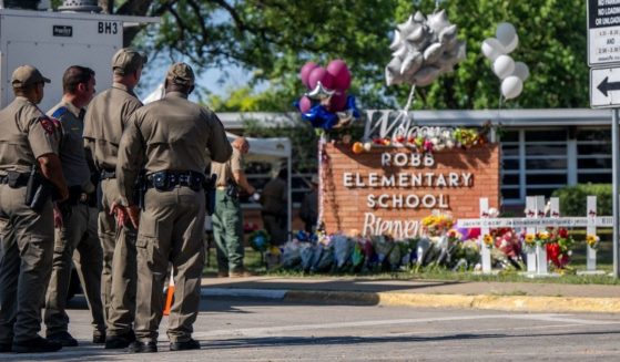 A memorial stands outside Robb Elementary School in Uvalde, Texas, with four law enforcement officers looking on.