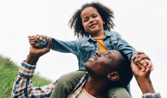 A boy sits on his father's shoulders in this stock image.