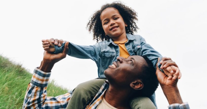 A boy sits on his father's shoulders in this stock image.