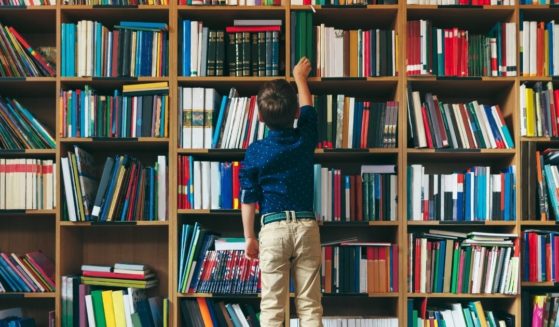 A boy reaches for a book in a library in the above stock image.