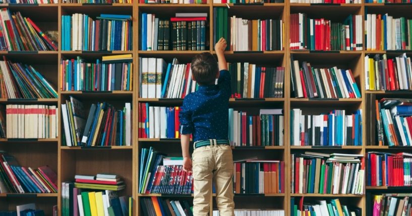 A boy reaches for a book in a library in the above stock image.