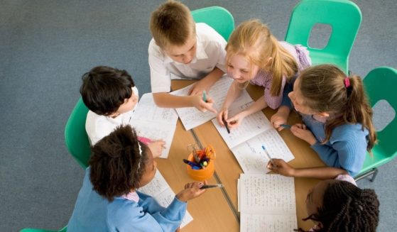 Children gather around a table while at school.