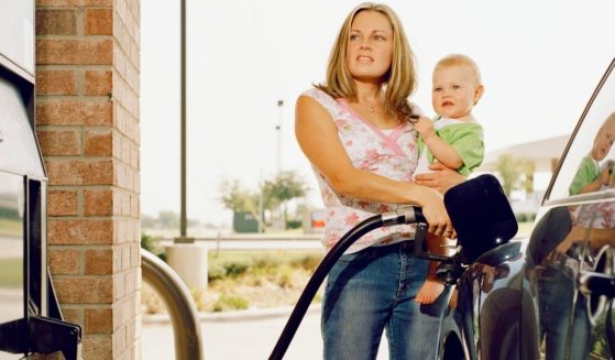 A mother holds her baby while pumping gas in this stock photo.