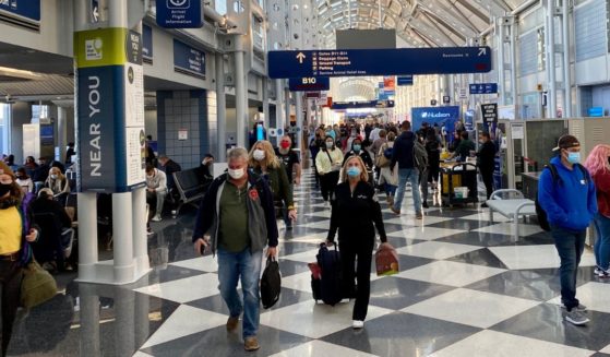 Travelers at Chicago O'Hare International Airport wear masks as they walk through and sit in the terminal.