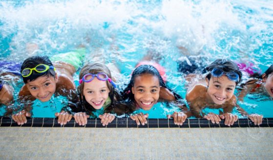 A group of elementary school children smile as they swim in a pool.