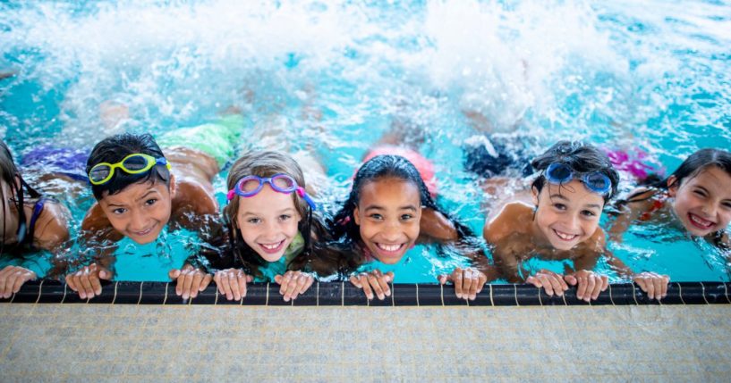 A group of elementary school children smile as they swim in a pool.